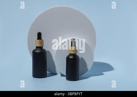 Natürliches ätherisches Öl oder Serum in schwarzen Glasflaschen auf einem runden Podium. Alternative Medizin, Schönheits-Hautpflegeprodukt. Speicherplatz kopieren. Blauer Hintergrund Stockfoto