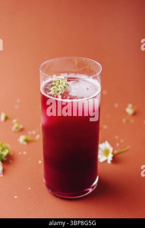 Essen, leuchtender Smoothie mit roten Beeren in einem hohen Glas, dekoriert mit kleinen weißen Blumen vor einem orangen Hintergrund Stockfoto