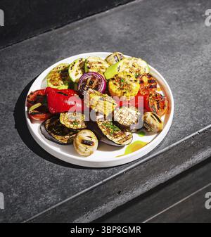 Speisen, Eine lebendige Auswahl an gegrilltem Gemüse ist kunstvoll auf einem weißen Teller angeordnet und präsentiert Zucchini, Mais, Zwiebeln und Paprika. Das Gericht ist se Stockfoto