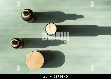 Gesichtsöl in schwarzen Tropfflaschen, geschlossene Feuchtigkeitscreme im Glasgefäß und flüssiges Serum mit Pipette auf grünem Hintergrund. Konzept der Naturkosmetik. Stockfoto