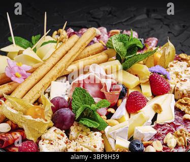 Speisen, Eine lebendige Käse- und Wurstplatte mit verschiedenen Käsesorten, Wurstwaren, frischem Obst, Nüssen und Kräutern, schön arrangiert für eine Freude Stockfoto