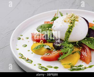 Speisen, lebendiger Caprese-Salat mit Burrata, Tomaten und frischem Basilikum-Pesto auf einem weißen Teller Stockfoto