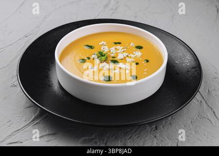 Speisen, samtige Kürbissuppe garniert mit Kräutern und Samen, serviert in einer stilvollen Schüssel auf einem schwarzen Teller Stockfoto