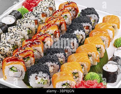 Speisen, diese raffinierte Sushi-Platte bietet eine Auswahl an lebhaften Brötchen, darunter Regenbogen-, Lachs- und Gemüsesorten, die wunderschön angeordnet sind Stockfoto
