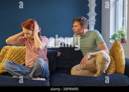 Unglückliches Paar streitet zu Hause auf der Couch. Ein verärgerter Ehemann, der eine verärgerte Frau angeschrien hat, die die Ohren schließt. Frau ignoriert emotional aufdringliche Husba Stockfoto
