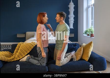 Negative Emotionen Paare. Ehemann und Ehefrau streiten und schreien, ausdrucksstarkes, emotionales, zerstrittenes Haus, das auf der Couch steht. Mann und Frau knieten vor Stockfoto