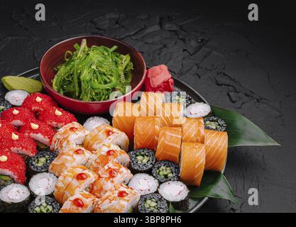 Essen, Eine wunderschön angeordnete Platte bietet verschiedene Sushi-Brötchen, einschließlich Lachs und Gemüse, sowie eine Schüssel mit lebendigem Algensalat Stockfoto