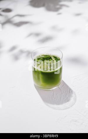 Essen, erfrischende Eismatcha Latte sitzt auf einem weißen Tisch mit Schatten von Blättern im Hintergrund Stockfoto