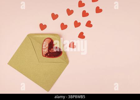 Papierhandwerk Umschlag mit streuenden roten Herzen auf rosa Hintergrund. Mit Kopierbereich. Kreatives Layout für den Valentinstag Stockfoto