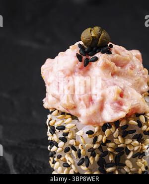 Speisen, kunstvoll präsentierte scharfe Thunfisch-Sushi-Rolle, garniert mit Sesamsamen auf einem dunklen Schieferhintergrund Stockfoto
