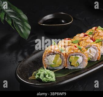 Speisen, kunstvoll präsentiertes Sushi auf einem eleganten, schwarzen Teller, komplett mit Essstäbchen und Sojasauce Stockfoto