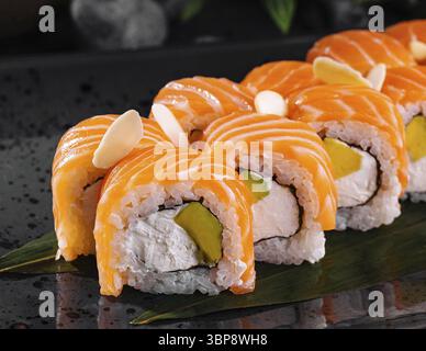 Speisen, Sushi-Brötchen mit Lachs, Avocado, Frischkäse und Gurke werden auf einem schwarzen Teller serviert Stockfoto