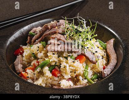 Essen, exquisite Schüssel Rindfleisch gebratenen Reis mit Gemüse, garniert mit Mikrogrün, serviert mit Essstäbchen Stockfoto
