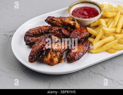 Essen, köstliche gebratene Hähnchenflügel mit goldenen Pommes frites und Ketchup auf einem weißen Teller Stockfoto