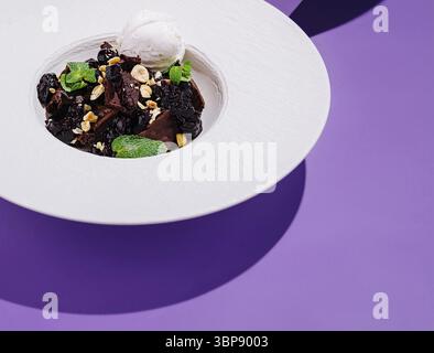 Essen, Ein Dessert aus reichhaltigen Schokoladen-Brownie-Stücken, garniert mit zerstoßenen Nüssen, Minzblättern und einem Löffel Vanilleeis wird elegant in einem W präsentiert Stockfoto