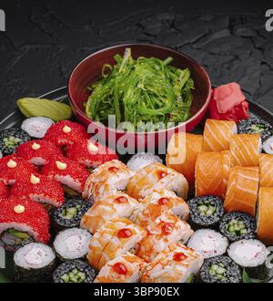 Speisen, Eine lebendige Sushi-Platte bietet eine Auswahl an bunten Brötchen, darunter hellrote Beläge und frische Lachsscheiben, begleitet von einer Schüssel gr Stockfoto