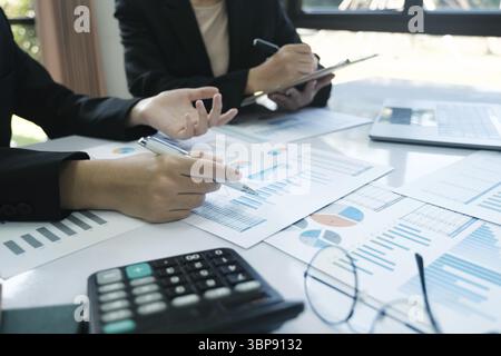 Zwei Leute sitzen an einem Tisch mit vielen Papieren und einem Taschenrechner. Sie arbeiten an einigen Finanzdaten Stockfoto