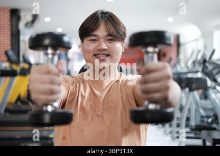 Ein Mann hält zwei Kurzhanteln in der Hand und lächelt. Er ist in einem Fitnessstudio Stockfoto