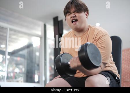 Ein Mann hebt Gewichte und ist sehr wütend. Er trägt ein orangefarbenes Hemd und schwarze Shorts Stockfoto