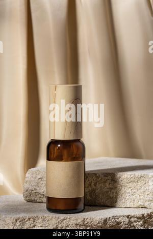 Bernsteinfarbene Glasflasche mit leerem Etikett, Creme auf einem Natursteinständer auf beigefarbenem Stoff Vorhänge Hintergrund. Natürliches Bio-Spa-Kosmetikmodell. Minimal Stockfoto