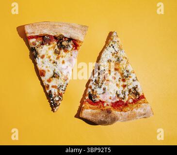 Essen, zwei leckere Stücke Pizza ruhen auf einer hellgelben Oberfläche. Eine Scheibe enthält Peperoni und Käse, während die andere mit verschiedenen Belägen versehen ist Stockfoto