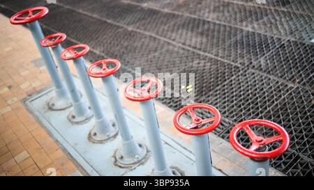 Reihe alter Retro-Ventilräder, rot lackiert, selektiver Fokus mit Verlängerungsvorrichtung über gefliestem Hintergrund und perforiertem Metallblech Stockfoto