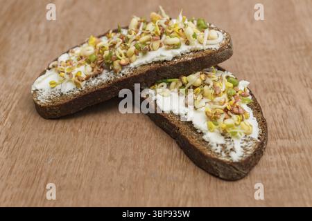Nahaufnahme von Roggenbrot-Sandwiches mit Frischkäse und gekeimten Mungbohnen, Walnuss, Sonnenblume und Flachs auf hölzernem Hintergrund. Vegane Rohkost-Diät Stockfoto