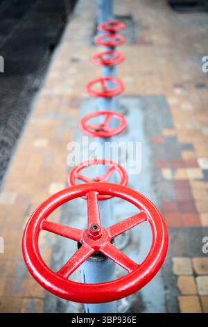 Reihe alter Retro-Ventilräder, rot lackiert, selektiver Fokus mit Verlängerungsvorrichtung über gefliestem Hintergrund und perforiertem Metallblech Stockfoto