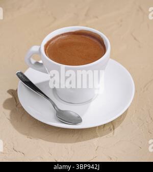 Essen, weiße Tasse Espresso-Kaffee auf Steinhintergrund mit Löffel und Untertasse Stockfoto