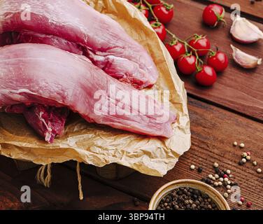 Das Essen, frisches Schweinefilet wird auf braunem Papier präsentiert, umgeben von lebhaften Kirschtomaten, Knoblauchzehen und einer Auswahl an Gewürzen. Das Settin Stockfoto