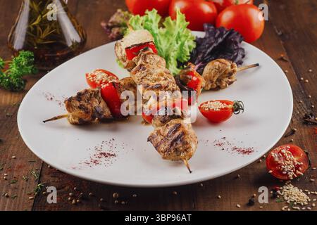 Speisen, gegrilltes Hühnchen und Paprikaspieße mit Gewürzen und Sesamsamen werden auf einem weißen Teller mit Kirschtomaten und Salat serviert Stockfoto
