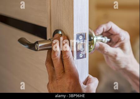 Mann, der den Türknopf repariert. Nahaufnahme der Hände des Arbeiters, der neuen Türschlosser installiert Stockfoto