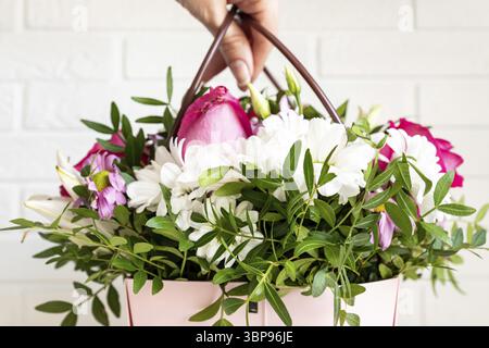 Eine Floristin, die eine schöne Blumenkomposition in einem Blumengeschäft herstellt. Frühlingsstrauß in rosafarbener Box mit Griffen Stockfoto