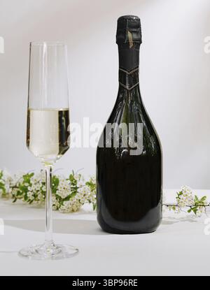 Essen, Eine elegante Flasche Sekt steht neben einem gefüllten Glas, beide elegant auf einem Tisch mit zarten weißen Blüten platziert, was eine Stockfoto