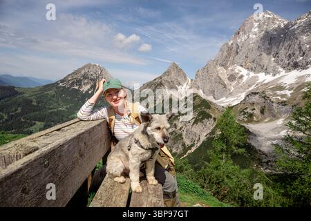 Lächelnde Frau mit Hund auf Bank in den österreichischen Alpen Stockfoto