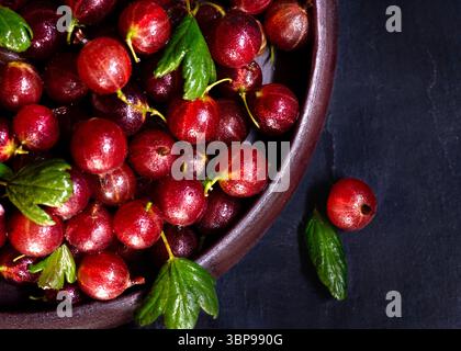 overhead  image of fresh seasonal organic ripe red gooseberries, rich ruby-red hue, dark slate surface, dramatic and rustic backdrop highlighting vivi Stockfoto