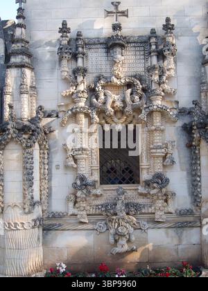 Ein detaillierter Blick auf ein kunstvoll verziertes Fenster auf einem Steingebäude mit komplizierten Schnitzereien und einem Kreuz auf der Spitze. Stockfoto