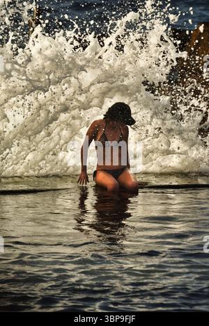 Attraktive Frau im Badeanzug, die sich bei Sonnenuntergang am natürlichen Swimmingpool entlang der Küste entspannt, Puerto de Santiago, Teneriffa, Kanarische Inseln, Spanien Stockfoto