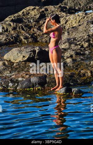 Attraktive Frau im Badeanzug, die sich bei Sonnenuntergang am natürlichen Swimmingpool entlang der Küste entspannt, Puerto de Santiago, Teneriffa, Kanarische Inseln, Spanien Stockfoto