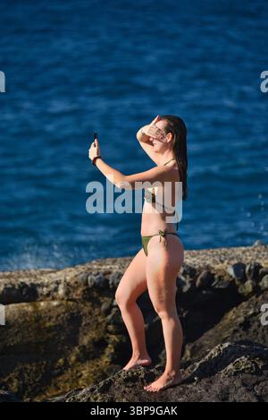Attraktive Frau im Badeanzug, die sich bei Sonnenuntergang am natürlichen Swimmingpool entlang der Küste entspannt, Puerto de Santiago, Teneriffa, Kanarische Inseln, Spanien Stockfoto