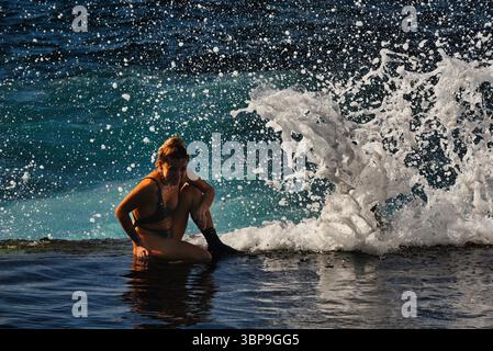 Attraktive Frau im Badeanzug, die sich während des Sonnenuntergangs am natürlichen Swimmingpool entlang der Küste entspannt, Charco de Isla Cangrejo, Teneriffa, Kanarische Inseln, Spanien Stockfoto