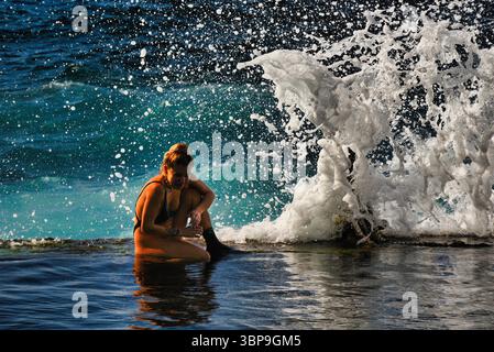Attraktive Frau im Badeanzug, die sich bei Sonnenuntergang am natürlichen Swimmingpool entlang der Küste entspannt, Puerto de Santiago, Teneriffa, Kanarische Inseln, Spanien Stockfoto