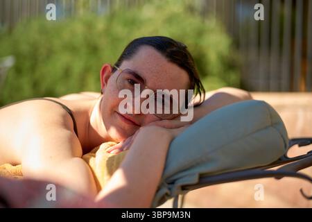 Eine Frau mit Brille entspannt sich draußen auf einem Liegestuhl, lehnt sich auf ein Kissen in der Sonne. Palm Springs, USA Stockfoto