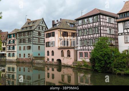 Traditionelle Fachwerkgebäude spiegeln sich in einem ruhigen Fluss unter einem bewölkten Himmel. Straßburg, Region Grand Est, Frankreich Stockfoto