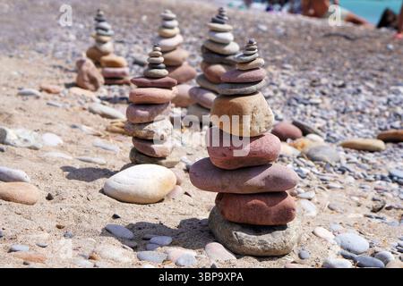 Haufen glatter Steine, die sorgfältig am Strand ausbalanciert sind, symbolisieren Meilensteine und Ruhe am Meer. Stockfoto