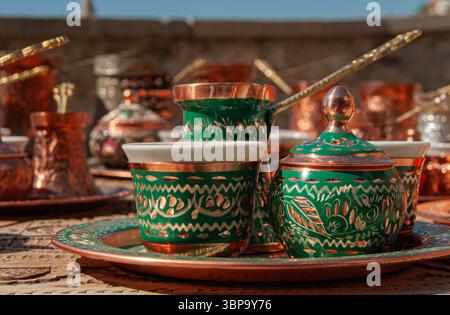 Traditionelle türkische Kupferkaffeekanne mit grüner Patina und passenden Tassen, bereit für die Zubereitung von reichhaltigem türkischem Kaffee. Stockfoto