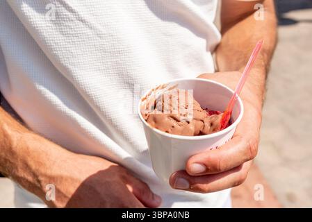 Mann, der eine Tasse mit einem Löffel süßem Dessert-Schokoladeneis in der Hand hält Stockfoto