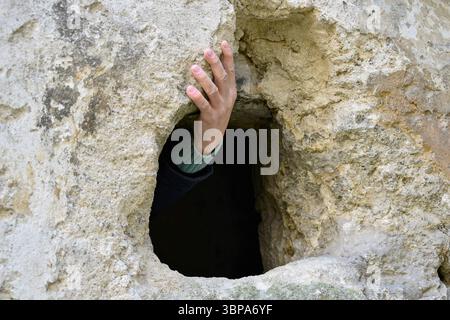 Die Hand des Mannes hält einen Steinvorsprung. Geheime Passage. Die alte, halb ruinierte Synagoge. Die Textur alter baufälliger Mauerwerke. Kopierbereich. Selektiver Fokus. Stockfoto