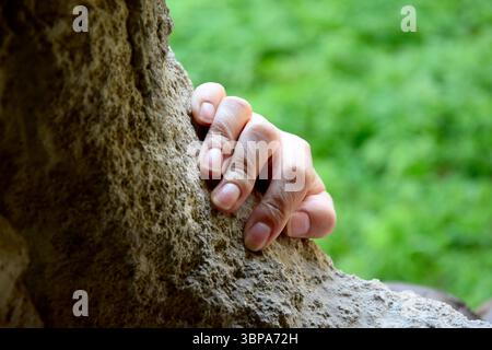 Die Hand der Frau, die einen Steinvorsprung vor grünem Hintergrund hält. Geheime Passage. Die alte, halb ruinierte Synagoge. Selektiver Fokus. Stockfoto