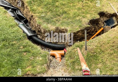 Rohrverlegung und Grabenaushub auf einem grasbewachsenen Rasen für die Installation von Drainage und Landschaftsgestaltung bei Neubauprojekten Stockfoto